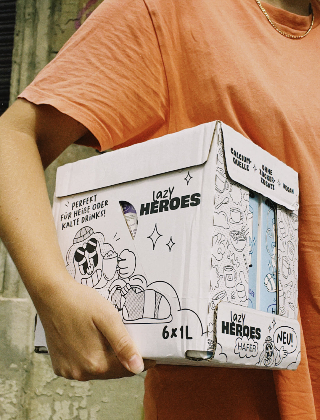 Eine Person hält eine Schachtel Hafer Allrounder mit einer Lazy-Helden-Zeichnung in der Hand.